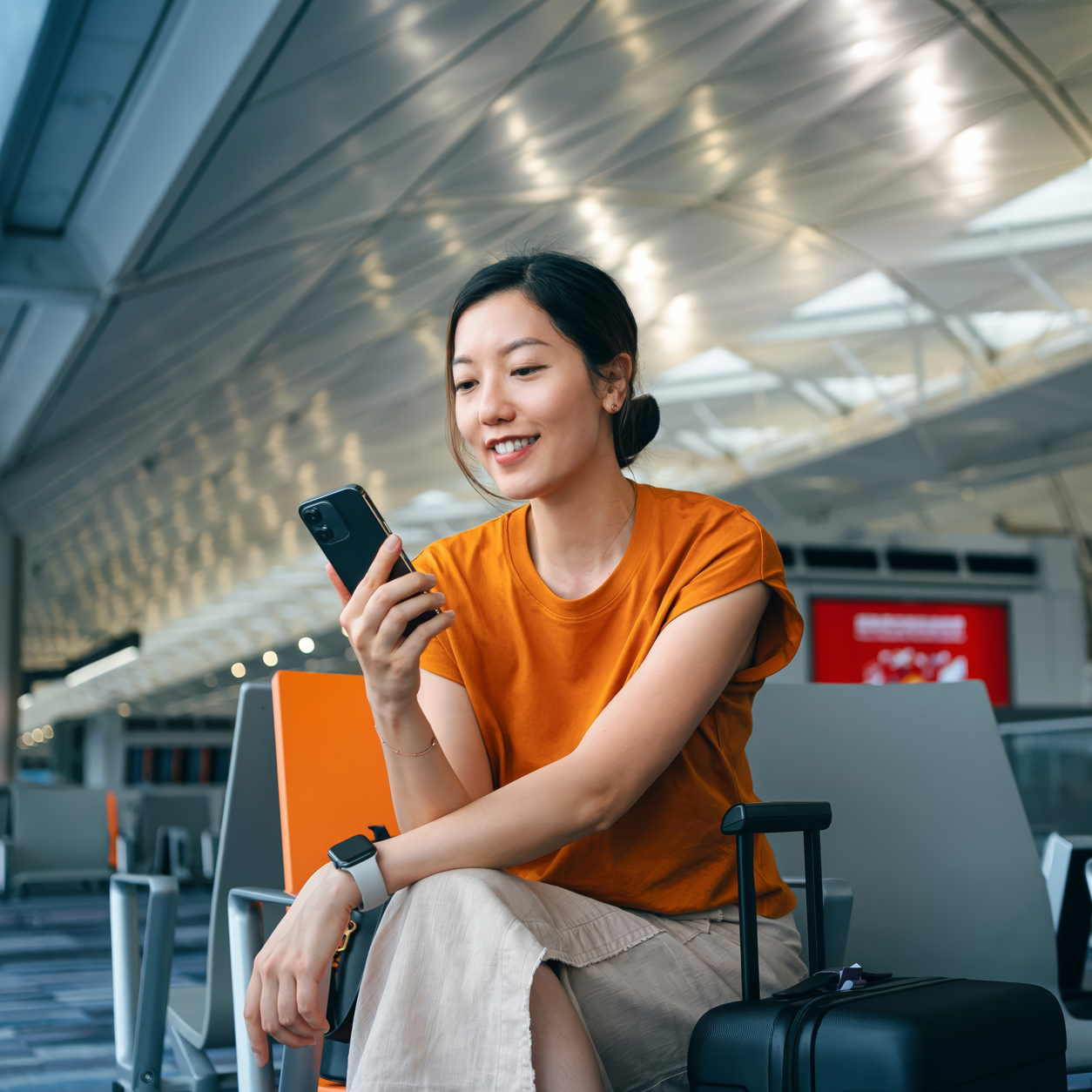 Woman in an orange shirt using her smartphone in an airport
